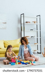 Young Nanny And Adorable Child Sitting On Floor In Living Room And Playing With Building Blocks