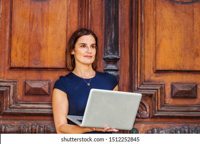 Young Native American Businesswoman Working In New York. Young Beautiful American Woman Wearing Short Sleeve Dress, Necklace, Working On Laptop Computer By Vintage Office Door, Looking Up, Thinking.
