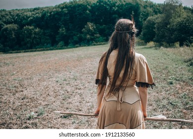 Young Native American Woman With A Spear Walking To The Forest, Indian Cosplay, Tribal Warrior Concept, Beautiful Young Girl In Indian Tribe Costume Posing With Back Turned To Camera