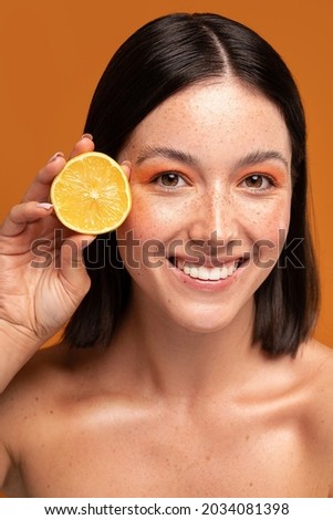 Young natural woman holding lemon near face, smiling and looking at the camera. Girl with freckles and perfect skin. 
