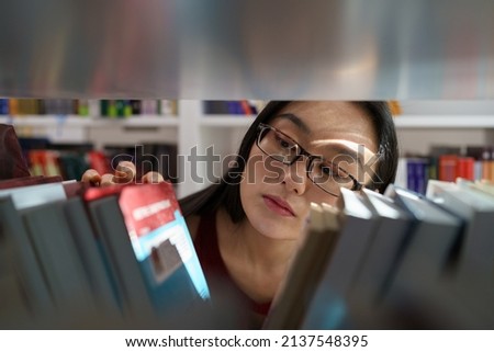 Young nerdy asian woman wearing glasses looking for academic journals, books and primary sources for research study while studying in university library. Effective literature searching and education