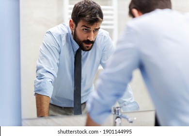 Young nervous attractive businessman leaning on the sink and looking himself in the mirror in restroom. - Powered by Shutterstock