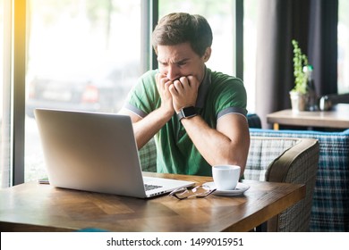 Young nervous businessman in green t-shirt sitting and working on laptop, bitting his nails and looking at screen with worry face. business and freelancing concept. indoor shot near window at daytime. - Powered by Shutterstock