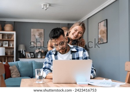 Young nervous college student man trying to learn and prepare for final exam while his girlfriend teasing him and making fun, trying to relax him. Freelance couple, job search male working on laptop