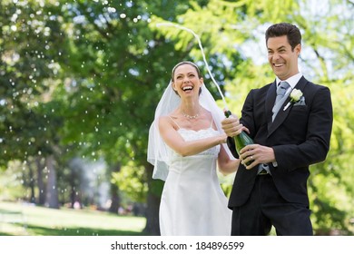 Young Newlywed Couple Popping Cork Of Champagne In Park