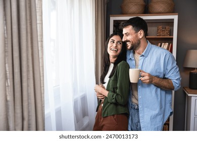 Young newlywed couple standing near window at their new apartment, enjoying their new life together. Engaged young people man and woman start living together, first day of their life in new home. - Powered by Shutterstock