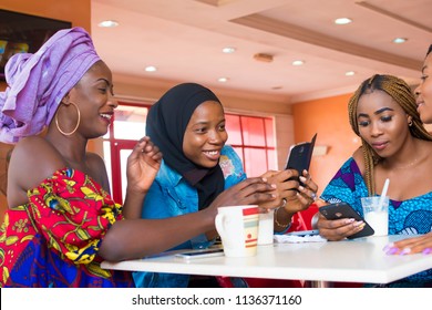 Young Nigerian Women Hanging Out Together In A Restaurant Smiling And Talking And Using Their Mobile Phones 