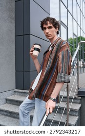 A young non binary individual sips coffee while lounging in an urban environment.