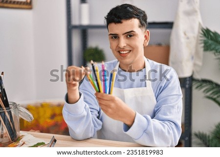 Young non binary man artist smiling confident holding color pencils at art studio