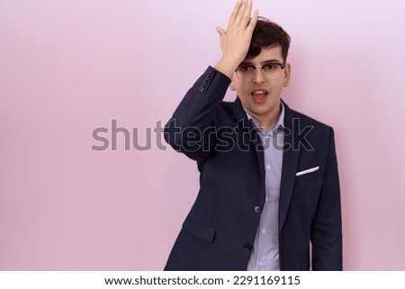 Young non binary man with beard wearing suit and tie surprised with hand on head for mistake, remember error. forgot, bad memory concept. 