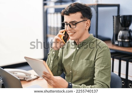 Young non binary man business worker talking on telephone reading notebook at office