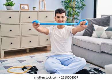 Young Non Binary Man Smiling Confident Using Elastic Band Training At Home