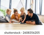 Young nuclear family playing with toys in a living room. Parents and children lying on floor, looking at children