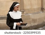 Young nun with Christian cross and Bible near building outdoors, space for text