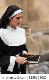 Young nun with Christian cross and Bible near building outdoors - Shutterstock ID 2258603623