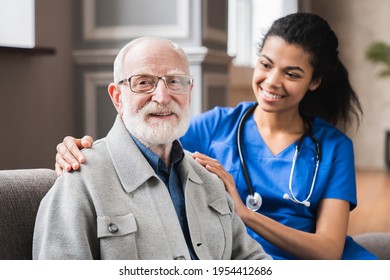 Young Nurse In Blue Coat Hugging Old 80s Man Smiling Looking At Camera. Portrait Of Satisfied Elderly Patient And His Caregiver. Medical Care Of Older Generation People, Nursing Concept