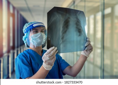 young nurse in a blue uniform protective mask and face shield looks at the result of lung fluorography