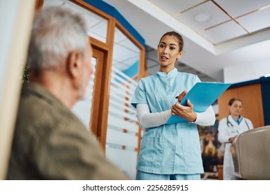Young nurse communicating with mature patient while writing his data in medical record at the clinic.  - Shutterstock ID 2256285915