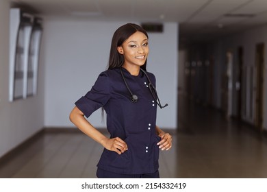 Young Nurse In Dark Blue Uniform And Stethoscope Over Her Neck. Portrait Of Female Nurse Wearing Scrubs In Hospital. Female Nurse Or Doctor Smiles Looking To Camera In Hospital Hallway
