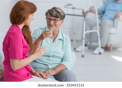 Young nurse drinking water and chatting with friendly senior woman - Powered by Shutterstock