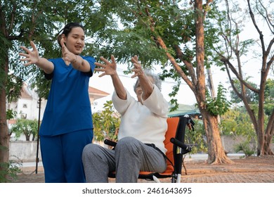 Young nurse and elderly asian senior woman on wheelchair, Asian careful caregiver and patient, stretches to exercise together for arm muscles at the garden on the evening. Health insurance. - Powered by Shutterstock