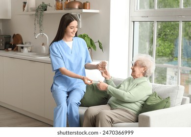 Young nurse giving pills and glass of water to senior woman in kitchen - Powered by Shutterstock