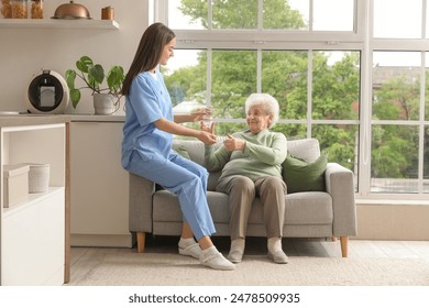 Young nurse giving pills and glass of water to senior woman in kitchen - Powered by Shutterstock