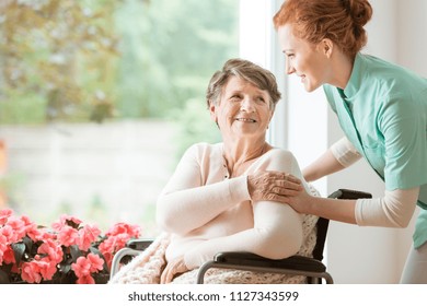 Young Nurse Helping An Elderly Woman In A Wheelchair. Nursing Home Concept