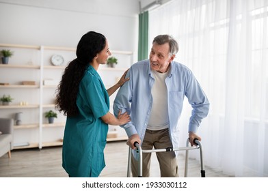 Young nurse helping older man to walk with frame at retirement home. Mature male petient with caregiver moving around at seniors centre. Professional eldercare service