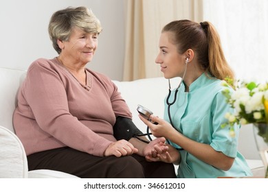 Young nurse measuring blood pressure of her senior lady patient