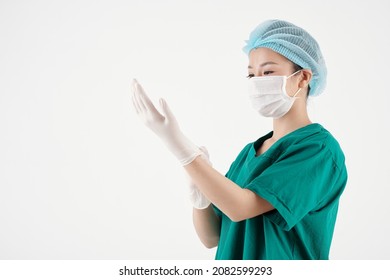 Young Nurse In Medical Hat And Protective Mask Putting On Rubber Gloves When Getting Ready For Work