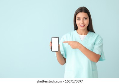 Young Nurse With Mobile Phone On Color Background