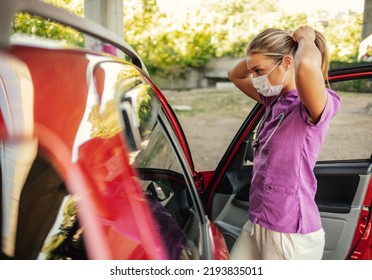 A Young Nurse Prepares For Her Shift At Work. A Nurse Dressed In Her Uniform Standing Outdoors In Front Of Her Car With A Mask On Her Face During The Day. 