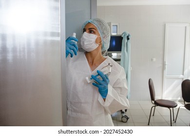 A Young Nurse In A Protective Suit, Cap, Mask And Gloves Takes Medications From A Locker In The Medical Office