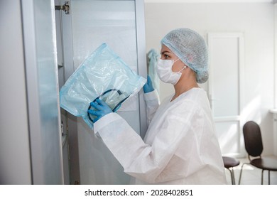 A Young Nurse In A Protective Suit, Cap, Mask And Gloves Takes Instruments From A Locker In The Medical Office