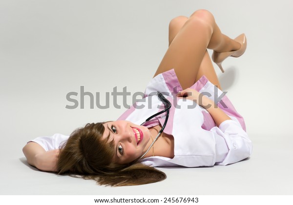 Young nurse in short medical gown with stethoscope lying on her back