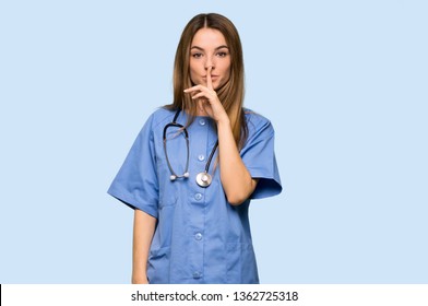 Young nurse showing a sign of silence gesture putting finger in mouth on isolated blue background