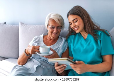 Young Nurse Spending Time With Happy Elder Patient In Nursing Home. Happy Senior Woman Talking With Friendly Nurse At Geriatric Ward 