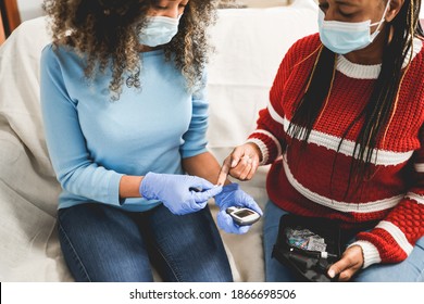 Young Nurse Takes Blood From A Senior African Patient For The Diabetes Exam While Wearing Surgical Mask For Coronavirus - Focus On Old Woman Right Hand 