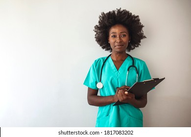 Young nurse using a clipboard against a grey background. Portrait Of Female Nurse Wearing Scrubs In Hospital. Female nurse or doctor smiles while staring out window in hospital hallway