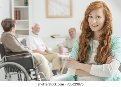 Young Nurse Watch Over Elderly People In Bright Common Room