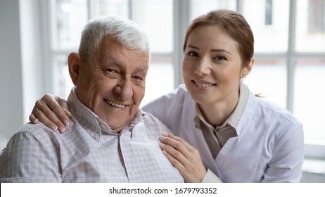 Young Nurse In White Coat Hugging Old 80s Man Smiling Looking At Camera. Portrait Of Satisfied Patient And His Caregiver. Medical Care Of Older Generation People, Geriatrics Medicine, Nursing Concept