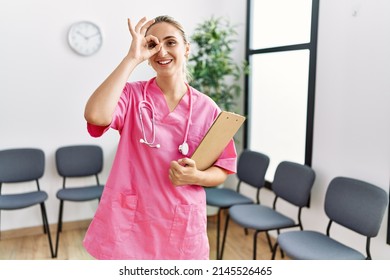 Young Nurse Woman At Medical Clinic Waiting Room Smiling Happy Doing Ok Sign With Hand On Eye Looking Through Fingers 