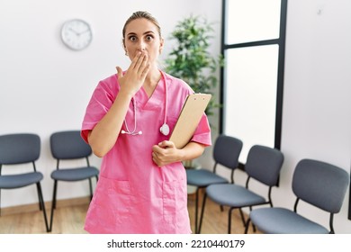 Young Nurse Woman At Medical Clinic Waiting Room Covering Mouth With Hand, Shocked And Afraid For Mistake. Surprised Expression 