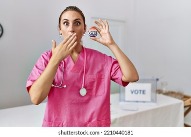 Young Nurse Woman At Political Campaign Holding Usa Vote Badge Covering Mouth With Hand, Shocked And Afraid For Mistake. Surprised Expression 