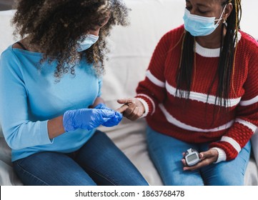 Young Nurse Woman Takes Blood From A Senior African Patient For The Diabetes Exam While Wearing Surgical Face Mask For Coronavirus