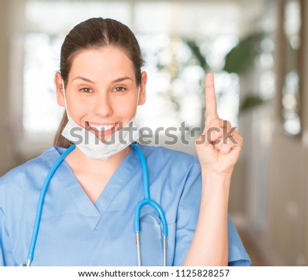 Young nurse woman wearing mask and stethoscope surprised with an idea or question pointing finger with happy face, number one