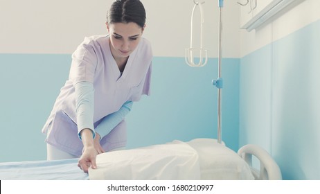 Young Nurse Working At The Hospital, She Is Cleaning Up The Room And Making The Bed