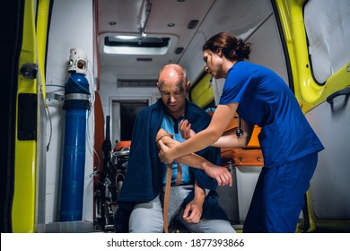 Young nurse wraps a tourniquet around a hand of her patient in an ambulance car.