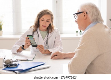 Young nutritionist giving recommendations about diet and trainings to senior patient while showing him data on smartphone screen - Powered by Shutterstock